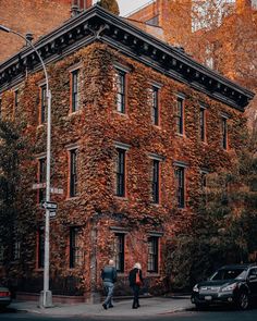 an old brick building with ivy growing on it's side and two people crossing the street