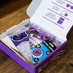 an open purple box with various items inside on a wooden table, including sunglasses and eyeglasses