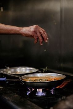 a person cooking food on top of a stove next to two frying pans