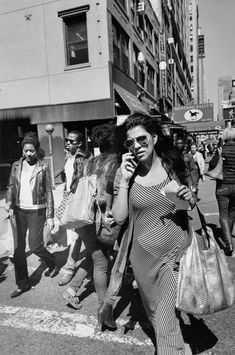 a woman walking down the street while talking on her cell phone and holding a purse