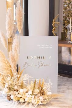 a white card with gold writing on it sitting on a table next to some flowers