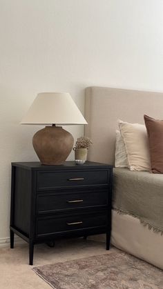 a lamp on top of a black dresser next to a bed with white sheets and pillows