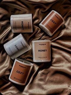 three different types of candles sitting on top of a bed next to each other with the words honey printed on them