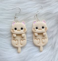 two cat shaped earrings on top of a white fur covered surface and one with black eyes