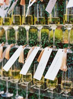 many wine glasses are lined up on the wall with tags attached to them and hanging from strings