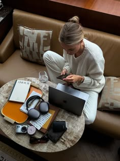 a woman sitting on a couch looking at her cell phone and laptop with headphones