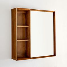 a wooden medicine cabinet with a mirror on the top and shelves below it, against a white wall