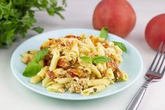 a blue plate topped with pasta and vegetables next to two red tomatoes on a white table