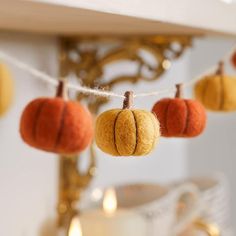 small felt pumpkins hanging from a string on a mantle or mantel with candles in the background