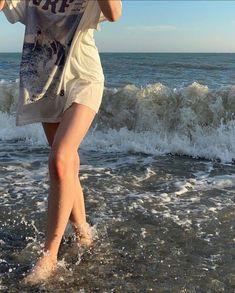 a woman is walking in the water at the beach with her cell phone to her ear