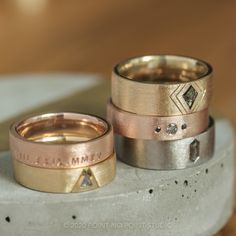 two gold and silver wedding bands sitting on top of each other, one with a diamond in the middle