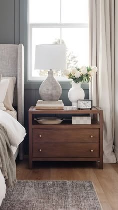 a bedroom with a bed, nightstand and lamp on the end table in front of a window