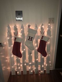 three stockings hanging on a fence with lights around them and the letters h above them