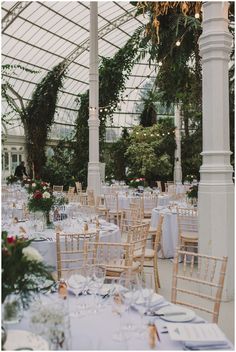 the tables are set for an elegant wedding reception in a glass walled building with white linens and floral centerpieces