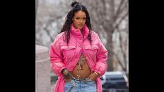 a woman in pink jacket and jeans standing next to a pillar with her hands on her hips