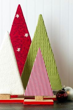 three small christmas trees are sitting on a table next to a red ornament