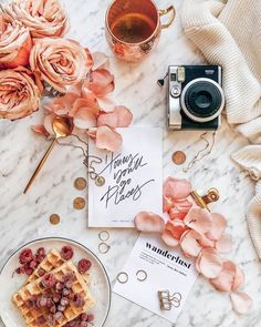 a table topped with pink flowers next to a plate of waffles and a camera