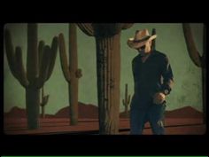 a man in a cowboy hat standing next to a cactus