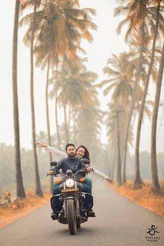 a man and woman riding on the back of a motorcycle down a road surrounded by palm trees