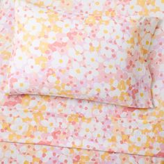 a bed with pink, yellow and white sheets on top of each other in front of a window