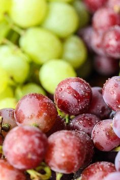 some grapes are sitting next to each other with water droplets on them and green leaves