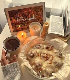 a person holding a coffee cup next to a plate of food and an open book