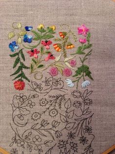 a cross stitch pattern with flowers and vines on it in a wooden hoop hanging from the wall