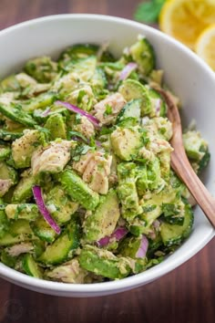 a white bowl filled with cucumber and red onions next to sliced lemons