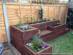 a wooden planter filled with lots of plants next to a fence and grass field