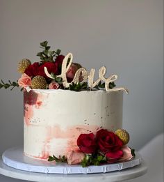 a white cake with red flowers and the word love on top is sitting on a table