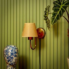 a lamp is on the wall next to a blue and white vase with a plant in it