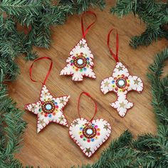 four ornaments hanging from a christmas tree on a wooden table with pine branches around them