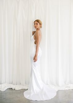 a woman standing in front of a white backdrop wearing a wedding dress and looking off to the side