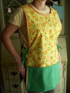 a woman standing with her hands on her hips wearing an apron and green shorts, smiling at the camera