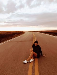 a woman is sitting on the side of an empty road with her feet in the air