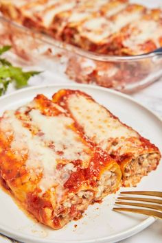 two slices of lasagna on a white plate with a fork and parsley