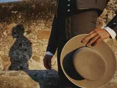 a man in a suit and hat standing next to a stone wall with his shadow on it