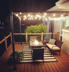 an outdoor patio with lights strung over the fire pit and seating on the back deck