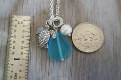 a blue sea glass necklace next to a coin and ruler on a wooden table with a penny