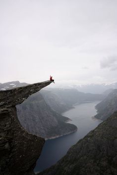 a man sitting on top of a cliff next to a lake in the middle of nowhere