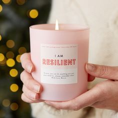 a woman holding a pink candle with the words i am resilint on it