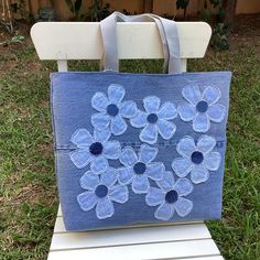 a blue bag with flowers on it sitting on a white chair in the grass next to a fence