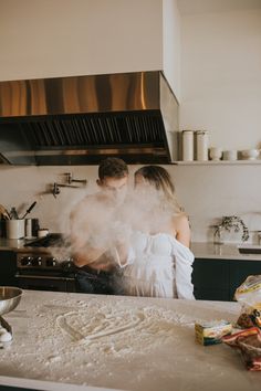 a man and woman standing in a kitchen with steam coming out of the stove top