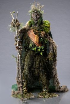 a man dressed up as a creature with plants on his head and arms, holding a stick