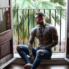 a man with tattoos sitting in front of a window