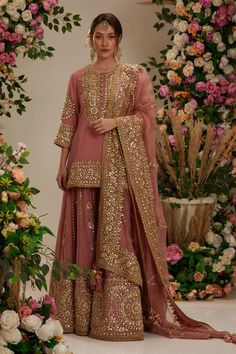 a woman standing in front of flowers wearing a pink outfit with gold sequins