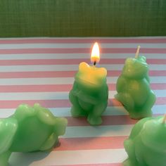 three green candles sitting on top of a pink and white striped tablecloth with a lit candle in the middle