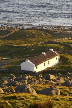 a small white house sitting on top of a lush green hillside next to the ocean