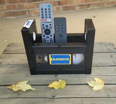 a remote control sitting in a black box on top of a wooden table next to leaves