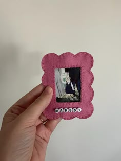 a hand holding up a small pink frame with a photo on the front and bottom